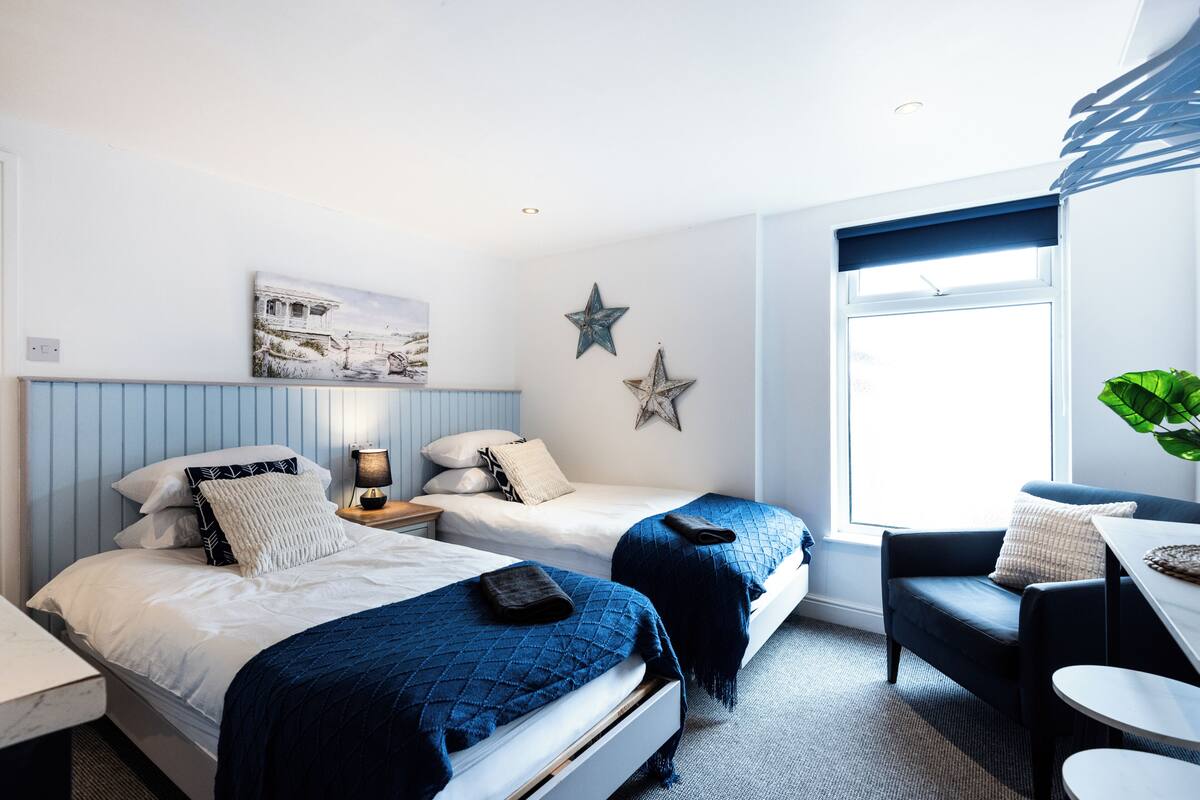 A bedroom with two beds, a desk, a chair, and a large window.
