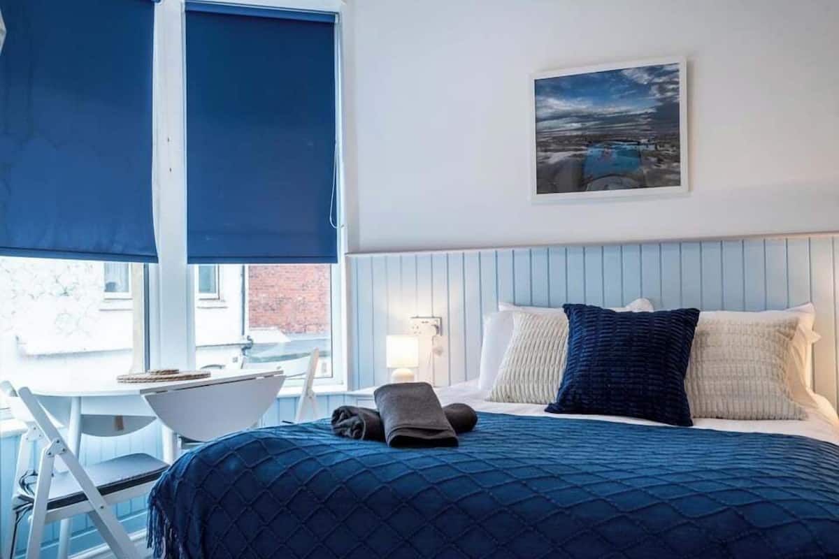A bedroom with a bed, pillows, a nightstand, a chair, and a window with a view.