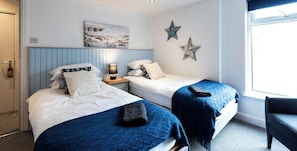 A hotel room with two beds, a nightstand with a lamp, a painting on the wall, and a window. - The Wellington Apart Hotel by Guestz (Blackpool)