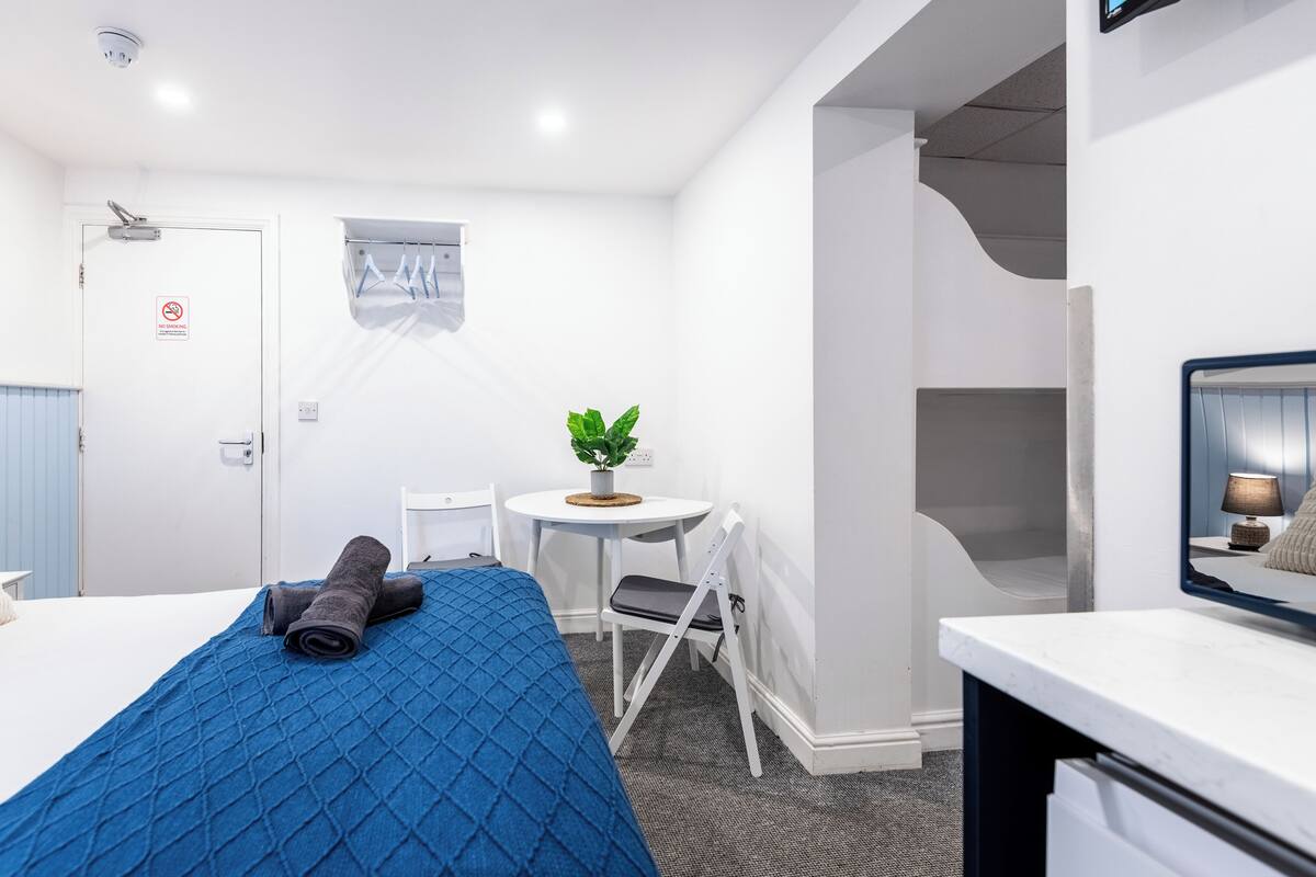 A hotel room with a bed, a small table with a plant, a chair, a desk, and a mirror.
