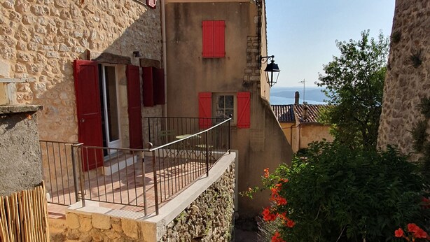 Un bâtiment en pierre avec des volets rouges, un balcon et une vue sur la mer.