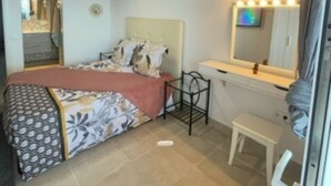 Ein Schlafzimmer mit einem Bett, einem Schminktisch mit Spiegel, einem kleinen Hocker und einer Decke mit Holzbalken.