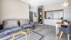 Uma sala de estar moderna com um sofá, uma mesa de jantar com cadeiras e uma área de cozinha com armários e bancada.