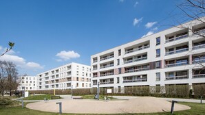 Um edifício de apartamentos moderno com várias varandas, um pátio central e céu azul claro.