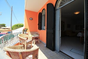 Ein Balkon mit Korbmöbeln, eine Tür zu einem Innenraum und ein klarer Himmel.