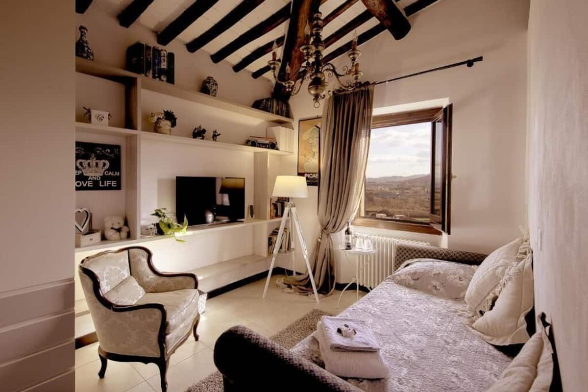 A room with a bed, a chair, a desk, and a window with a view.