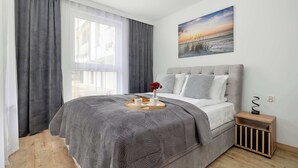 Ein Schlafzimmer mit Bett, Nachttisch, Fenster mit Vorhängen und einem Wandbild.