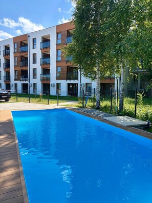 En modern lägenhetsbyggnad med pool, balkonger och en välskött trädgård.