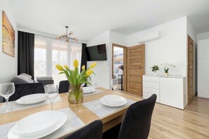 En matplats med ett träbord dukat för två personer, en vas med gula blommor och en platt-TV som är monterad på väggen.