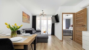 Ein modernes Wohnzimmer mit Essbereich, einem grauen Sofa, einem Holztisch und einem an der Wand befestigten Fernseher.