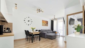 Ein modernes Wohnzimmer mit Essbereich, einem grauen Sofa, einem Holztisch und einer Wanduhr.