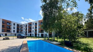 Ein modernes Mehrfamilienhaus mit Schwimmbad, umgeben von Bäumen und einem eingezäunten Parkplatz.
