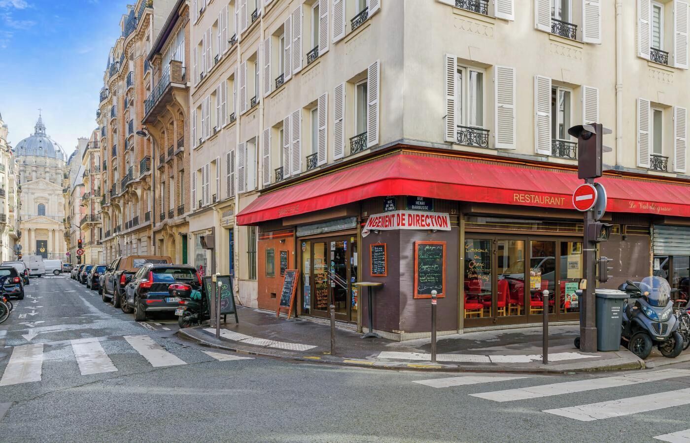 A street view with a restaurant named 'INGEMENT DE DIRECTION' with outdoor seating, parked cars, and a historic building in the background.