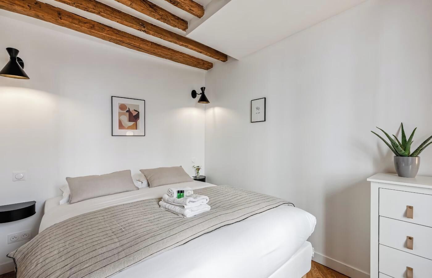 A modern bedroom with a bed, bedside tables, a potted plant, and artwork on the walls.