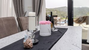 Een eettafel met een marmeren blad, een witte kaars, een glazen vaas met roze bloemen en een fles wijn.