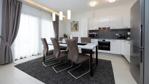 Een moderne keuken met witte kasten, een roestvrijstalen koelkast en een eethoek met een tafel en stoelen.