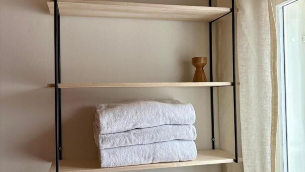 Un estante de pared con tres repisas, una de las cuales sostiene toallas dobladas.