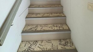 Una escalera con barandilla, peldaños alfombrados y una lámpara fijada a la pared.