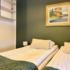 A bedroom with two beds, a painting on the wall, and a shelf unit.