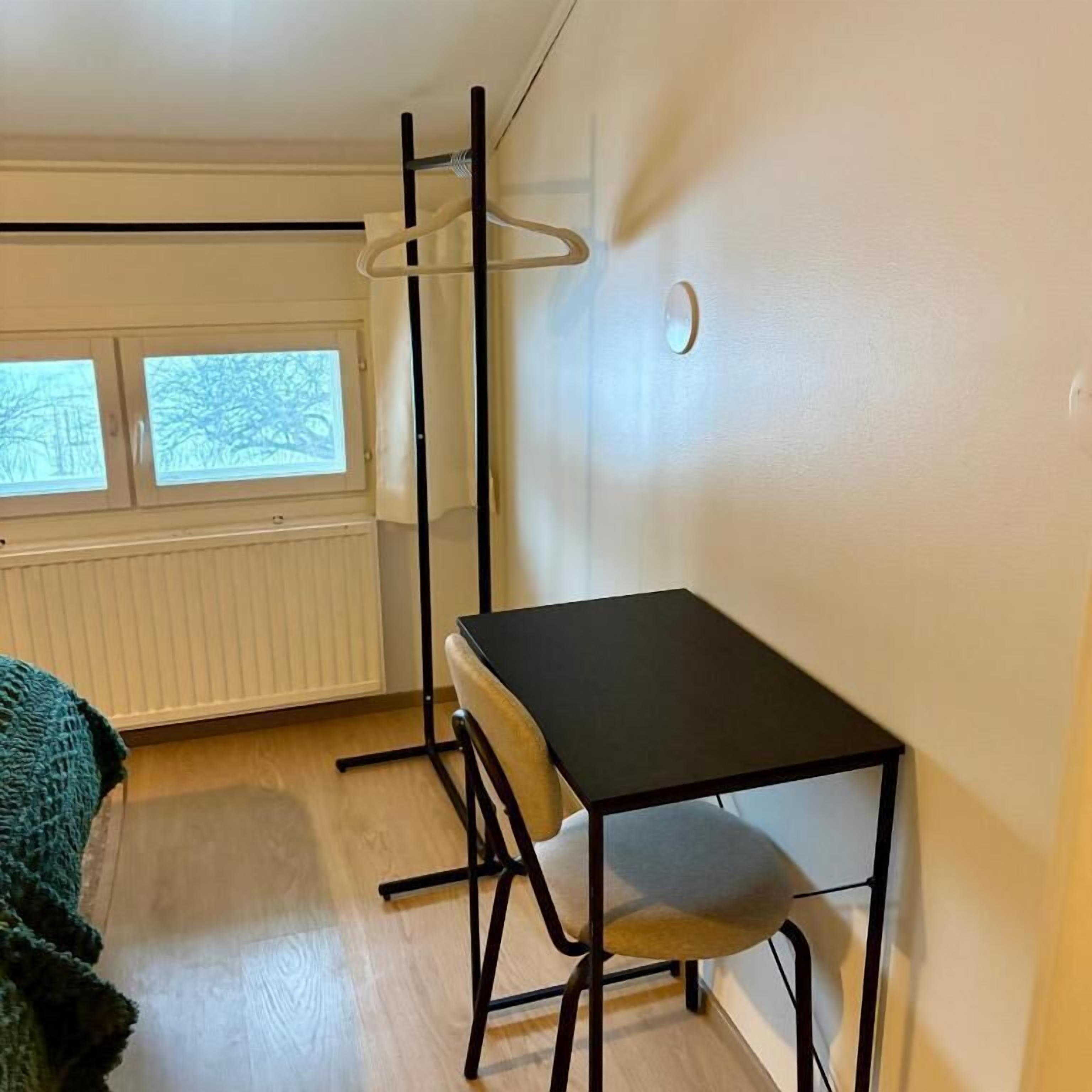 A room with a single bed, a small table, a radiator, and a window with a view.