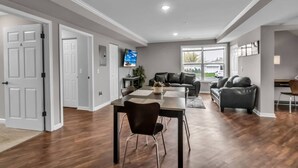 A spacious living room with a dining area, a gray couch, and a TV mounted on the wall.