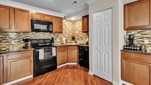 A kitchen with wooden cabinets, a black stove, a microwave, and a tiled backsplash.