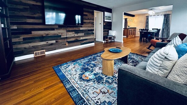 A modern living room with a wooden wall, a flat-screen TV, a round coffee table, and a sofa with cushions.
