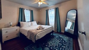 A bedroom with a bed, nightstand, mirror, ceiling fan, and patterned rug.