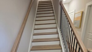 Eine Holztreppe mit Geländer, weißen Wänden und einer Tür oben.