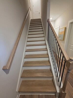 Eine Holztreppe mit Geländer, weißen Wänden und einer Tür oben.