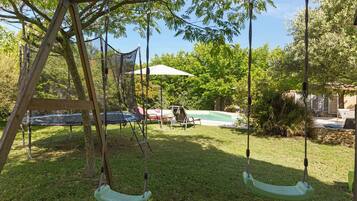 Ein Spielplatz aus Holz mit zwei Schaukeln, einem Pool und einer überdachten Terrasse im Garten.