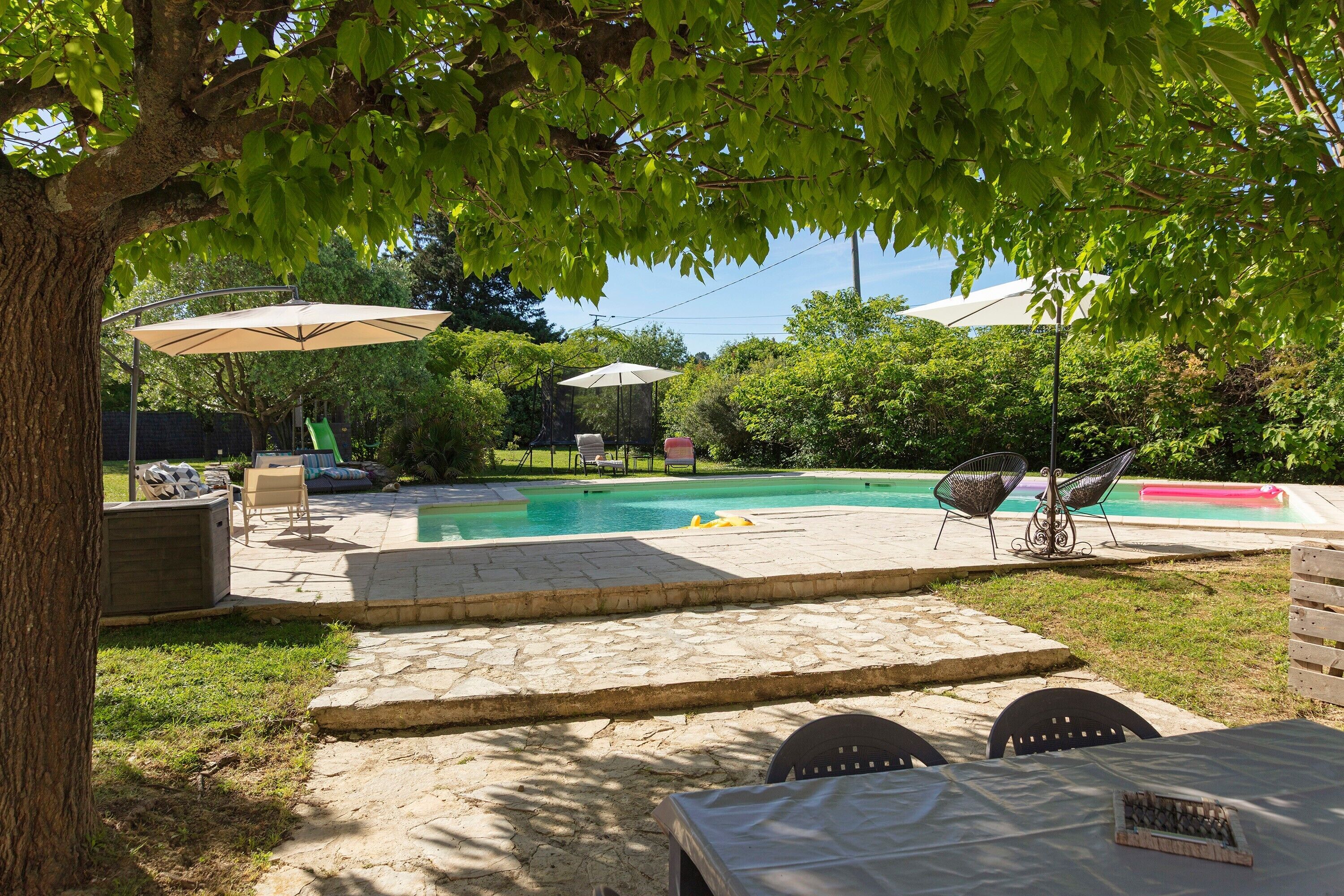 Um quintal com piscina, móveis de varanda e uma árvore que oferece sombra.