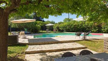 Um quintal com piscina, móveis de varanda e uma árvore que oferece sombra.