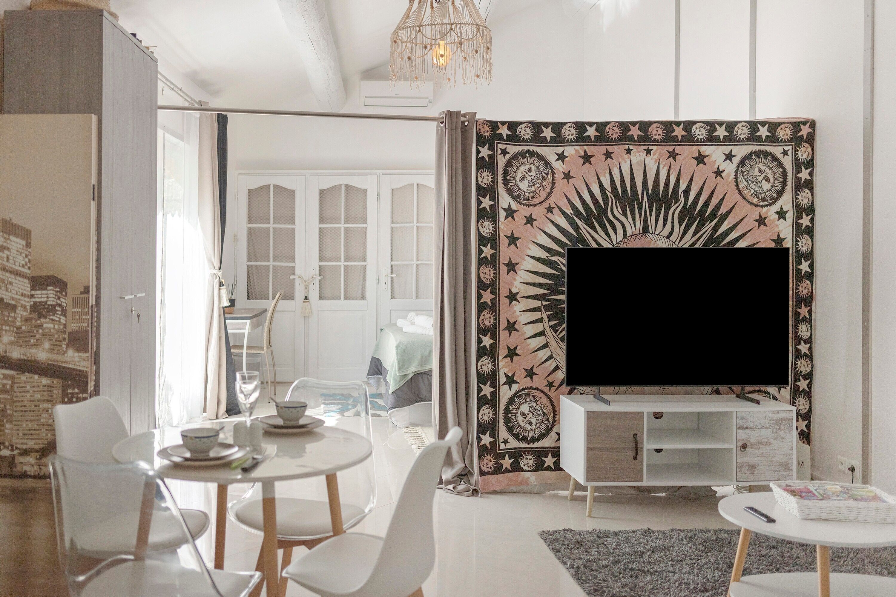 Een moderne woonkamer met een flatscreen televisie, een eethoek met stoelen en een tafel, en een wandtapijt met een patroon.