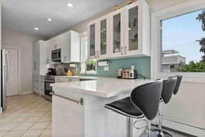 A modern kitchen with white cabinets, a central island, bar stools, and a large window.