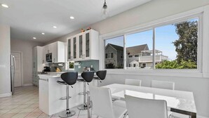 A modern kitchen with white cabinets, a central island, and a dining area with white chairs. - Beautiful Bayfront Home • Heated Pool & Jacuzzi (West Haven)
