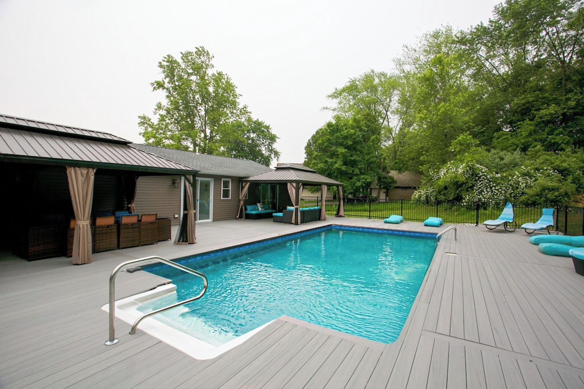 Ein Swimmingpool mit Sonnendeck, Liegestühlen und einer überdachten Sitzgelegenheit.