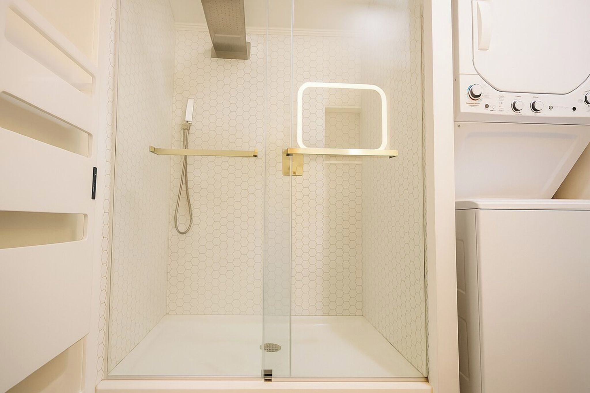A glass-enclosed shower with a handheld showerhead and a wall-mounted control panel.