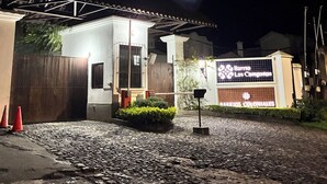 Un bâtiment doté d’une entrée fermée par un portail, d’une allée pavée et d’une enseigne indiquant qu’il s’agit d’un hôtel de style colonial.