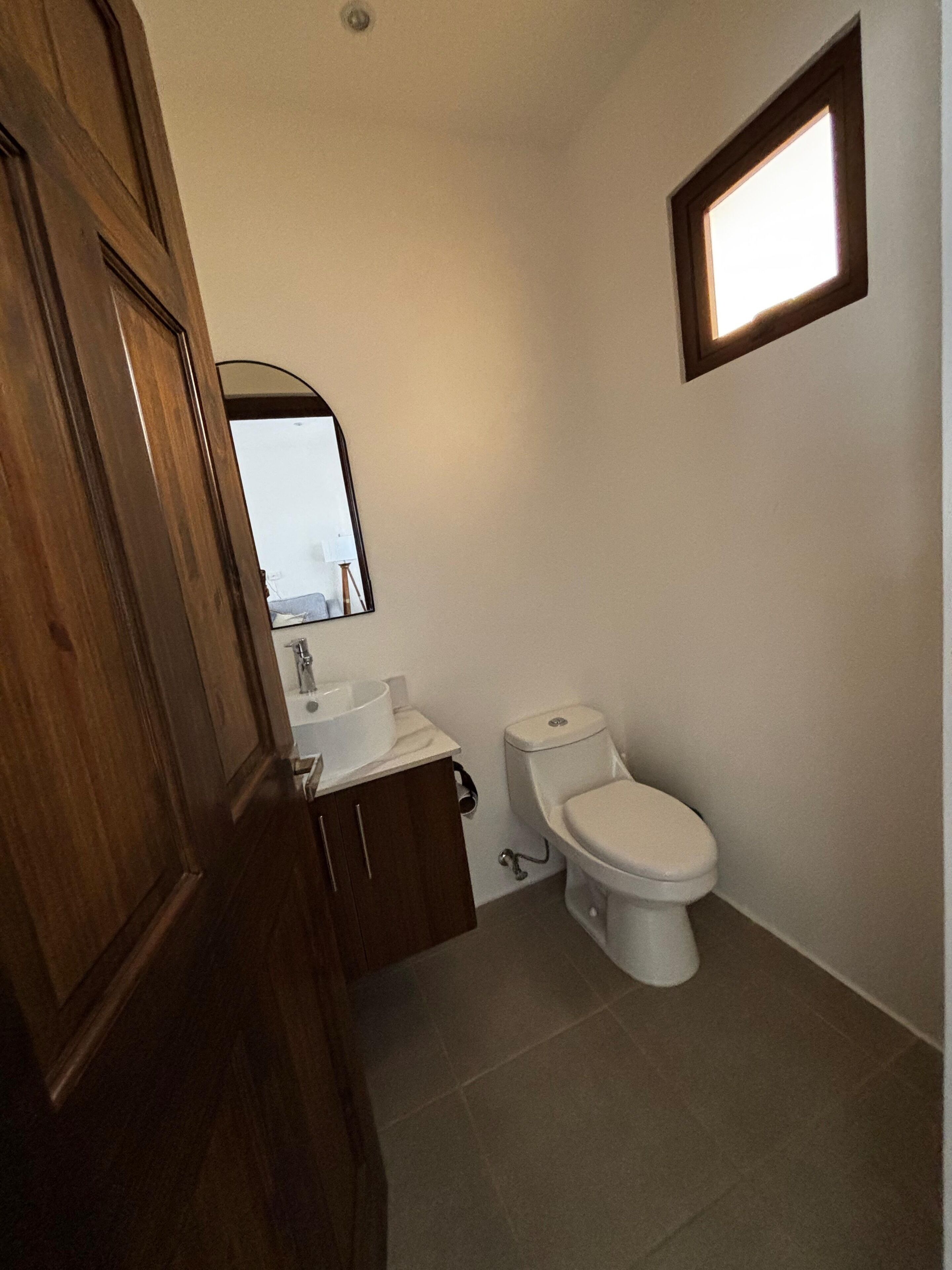Un baño con inodoro, lavabo, espejo y una ventana pequeña.