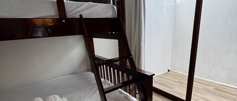 A bunk bed with white bedding and towels, a wooden floor, and a large window with curtains.
