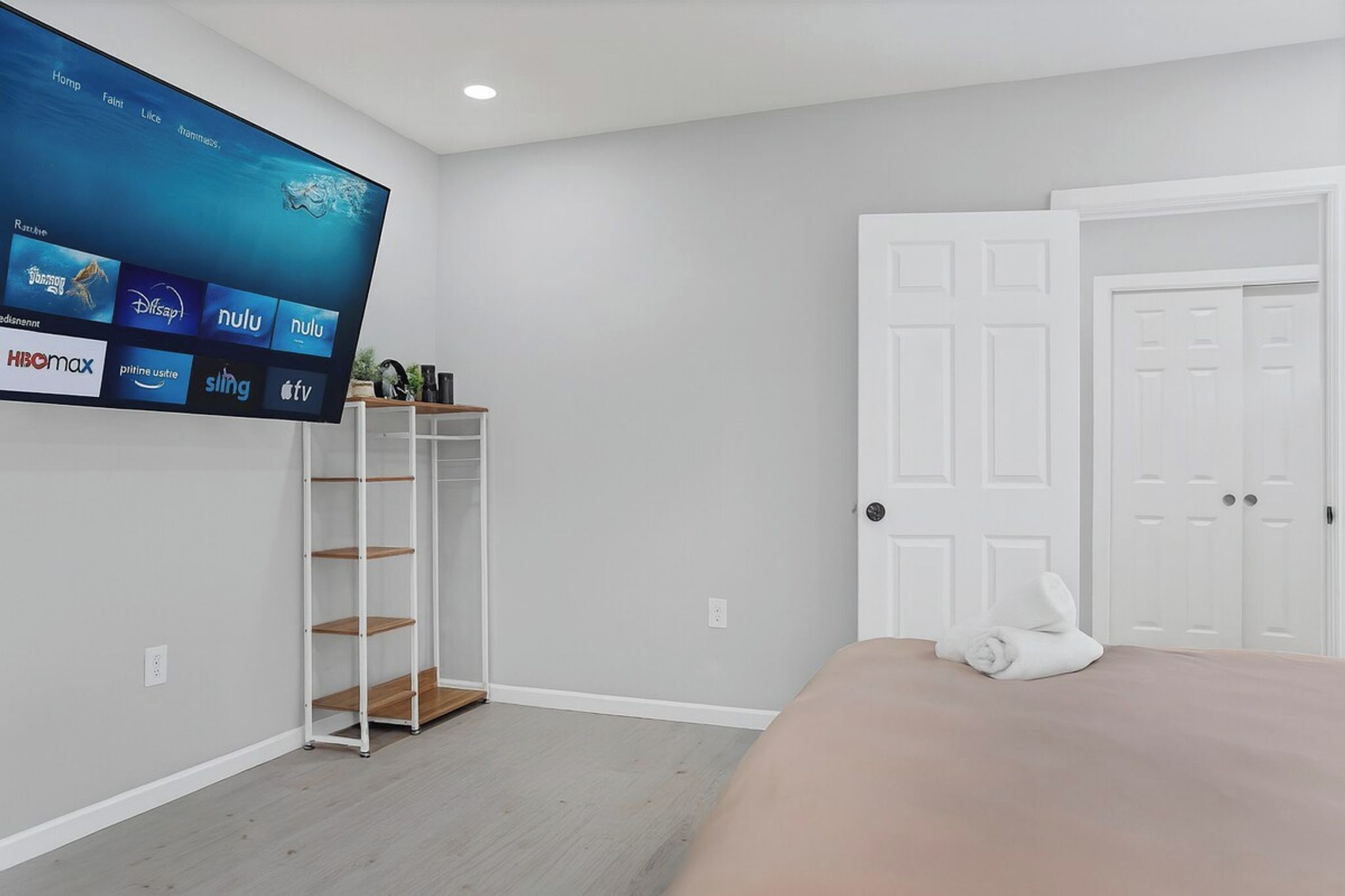 A bedroom with a bed, a TV mounted on the wall, a white door, and a white wardrobe.