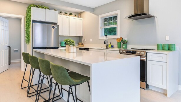 Una cocina moderna con armarios blancos, un refrigerador de acero inoxidable, una estufa a gas y taburetes verdes.