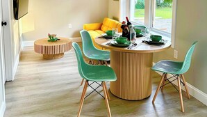 Un coin repas avec une table ronde en bois, des chaises vertes et un canapé jaune.