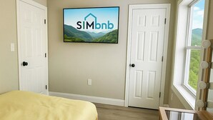 Une chambre à coucher avec un lit, un bureau doté d’un miroir, un téléviseur fixé au mur et deux portes.