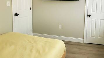 A bedroom with a bed, two doors, a mounted television, and a carpeted floor.