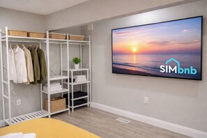 Una habitación moderna con un estante blanco, un televisor de pantalla plana mostrando un atardecer y el logotipo de SIMbnb.