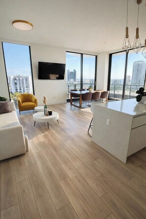 A modern living room with a sofa, a yellow armchair, a dining table, and a kitchen area with a white island. - Large 3BR / pool / gym / Jacuzzi / Sauna / grill (Hallandale Beach)