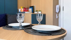 Taula de menjador amb dos plats i dues copes, paret de fusta, sofà blau i un telèfon a la paret.