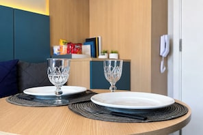 A dining table with two plates and two glasses, a wooden wall, a blue sofa, and a phone on the wall. - Premium Studio 5 min from CGH, Gym and Coworking (São Paulo)